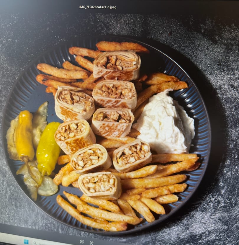 Small filled wraps, golden french fries, white dipping sauce, and pickled vegetables on a dark plate.