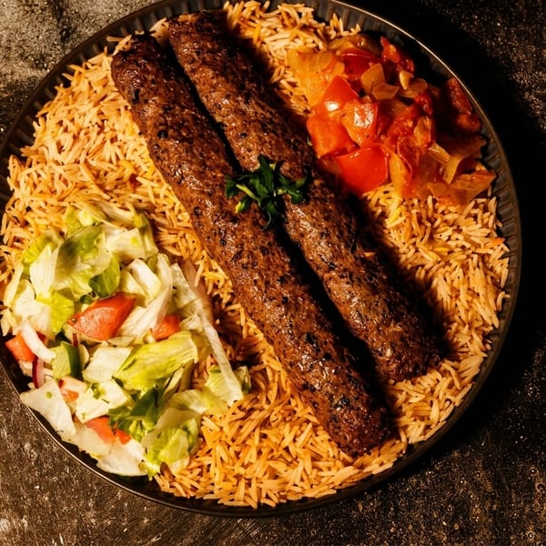 Two kebabs on a bed of rice with a side salad and cooked vegetables.