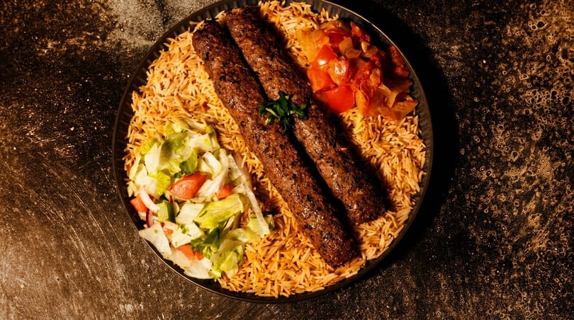 Two kebabs on a bed of rice with a side salad and cooked vegetables.