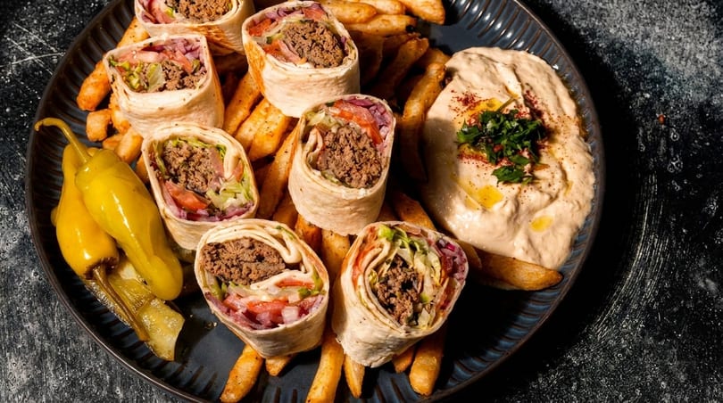 Beef shawarma wraps with fries, hummus, and pickled peppers on a dark plate.