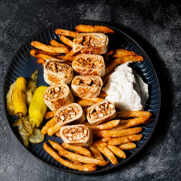 Chicken shawarma wraps, seasoned fries, pickled vegetables, and a white dipping sauce on a dark plate.