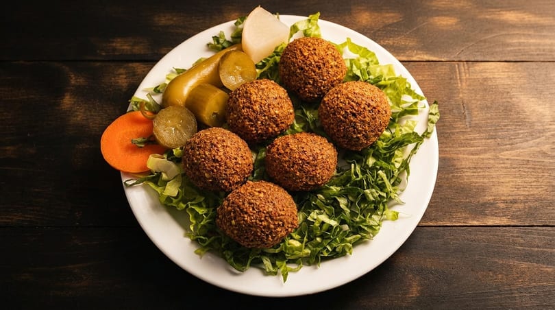 A plate of falafel balls on a bed of lettuce, with pickles, carrots, and radish.