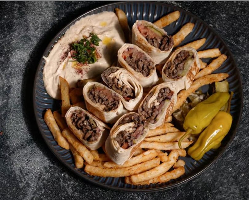 A plate of sliced shawarma wraps, golden fries, creamy hummus, and bright pickled peppers.