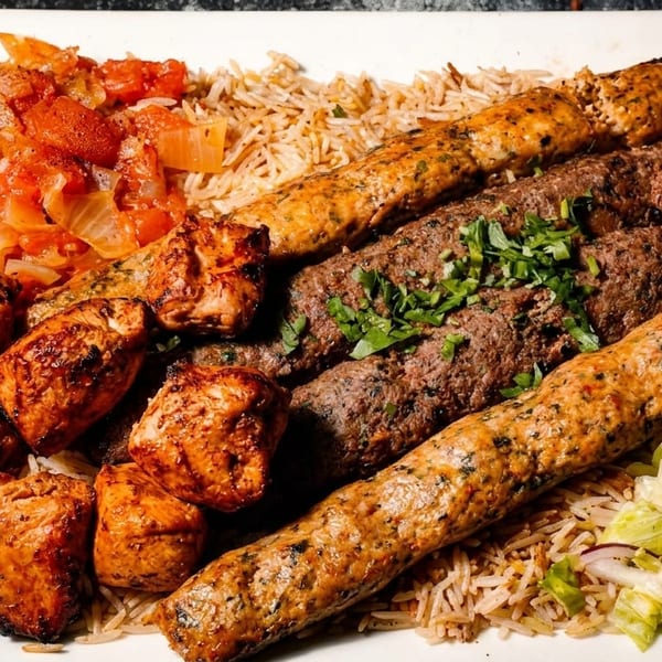 A platter of various grilled meats, rice, tomato stew, and salad on a white plate.
