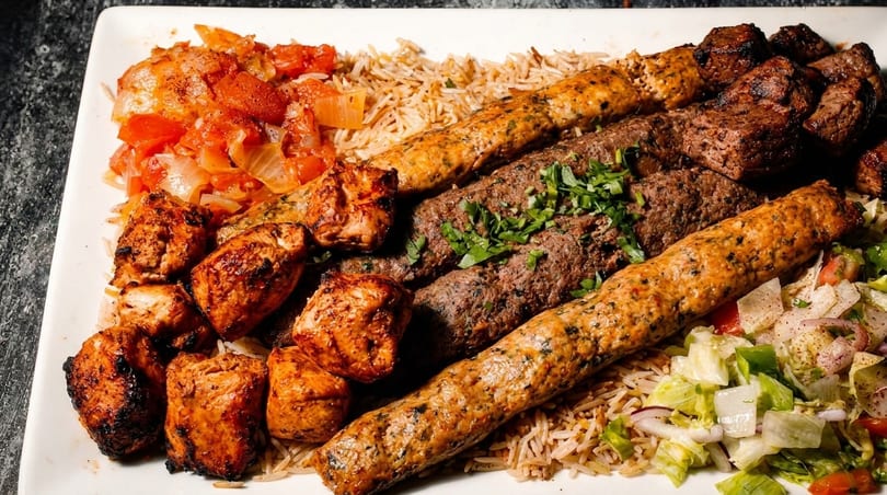 A large platter of grilled chicken, beef, and kofta kebabs with rice, tomato relish, and salad.