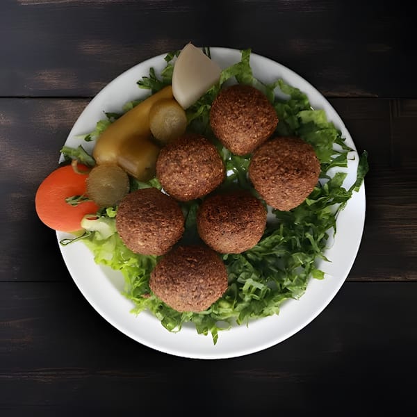 Six falafel balls on a bed of lettuce, with sliced tomatoes and pickles on a white plate.