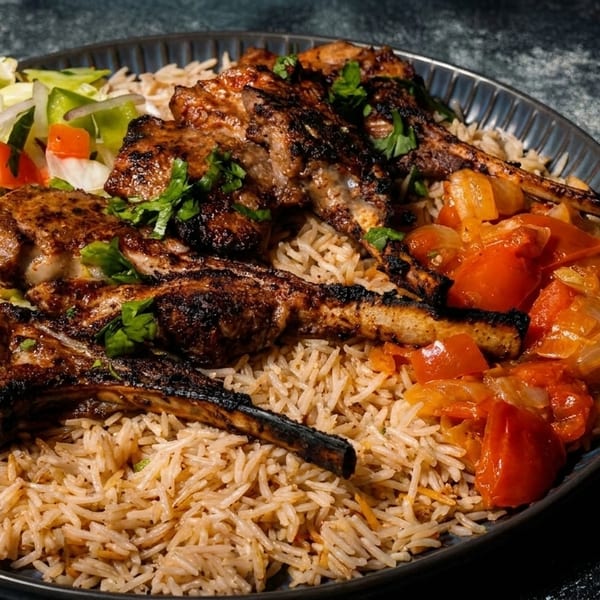 Grilled lamb chops with rice, fresh salad, and stewed tomatoes and onions on a dark plate.