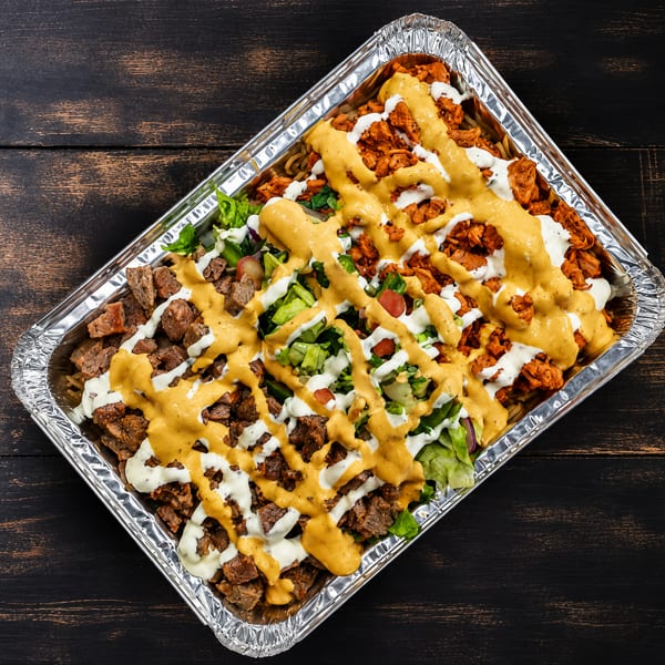 A foil tray filled with rice, chicken, beef, lettuce, tomatoes, and two sauces.