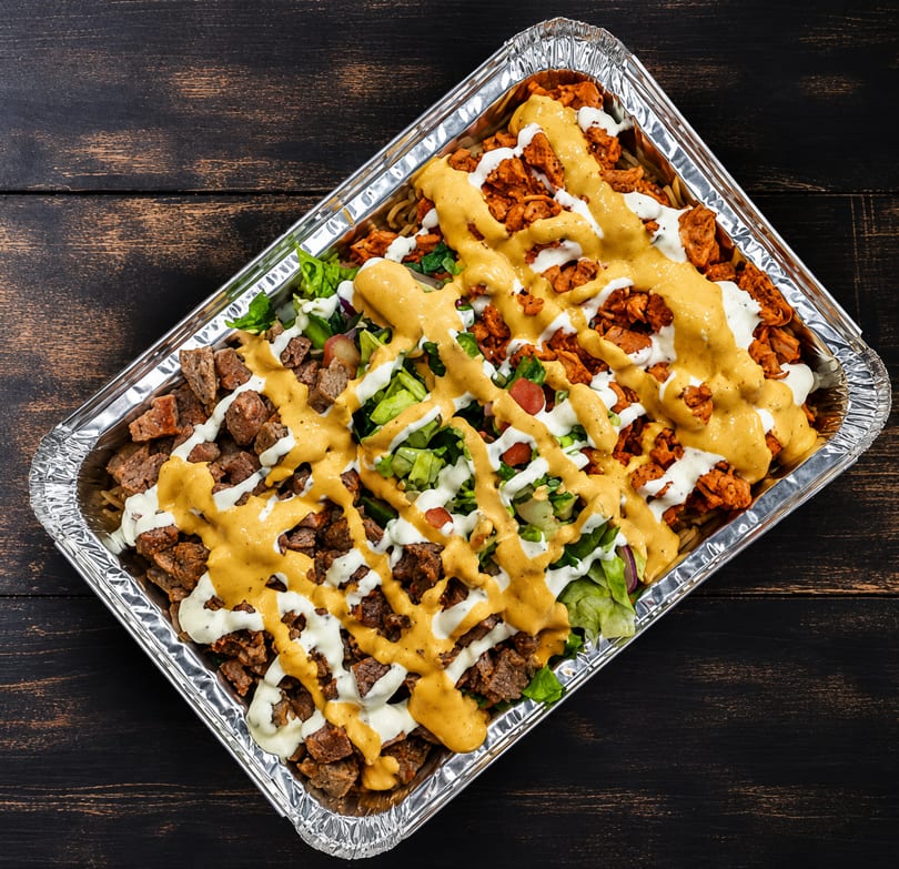 A foil tray filled with rice, chicken, beef, lettuce, tomatoes, and two sauces.
