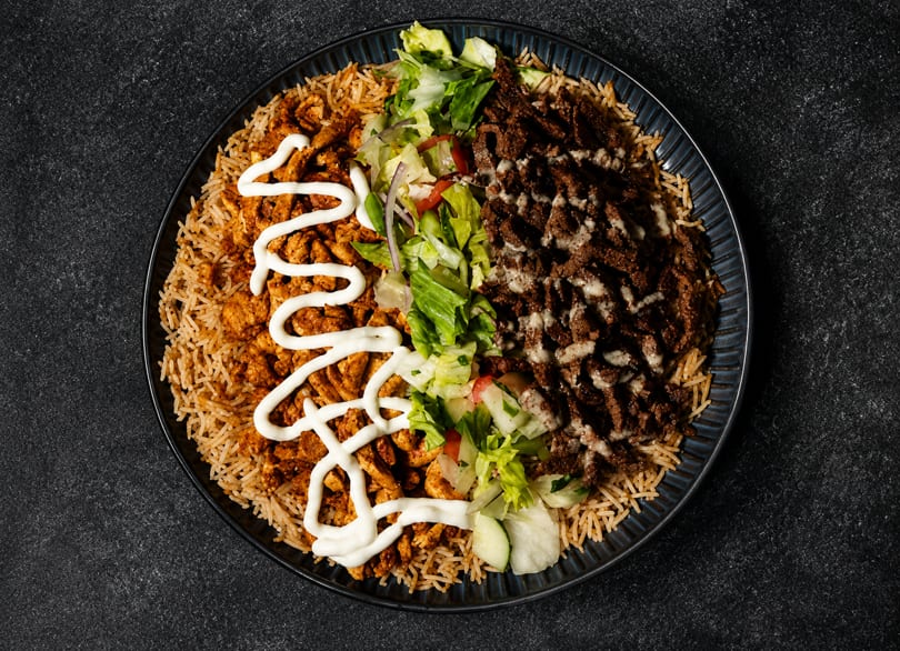 Delicious rice platter with chicken, beef, fresh salad, and white sauces.
